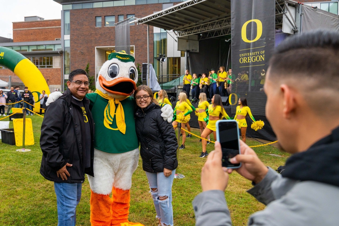 Man taking photo of student and parent posing with the UO Duck.